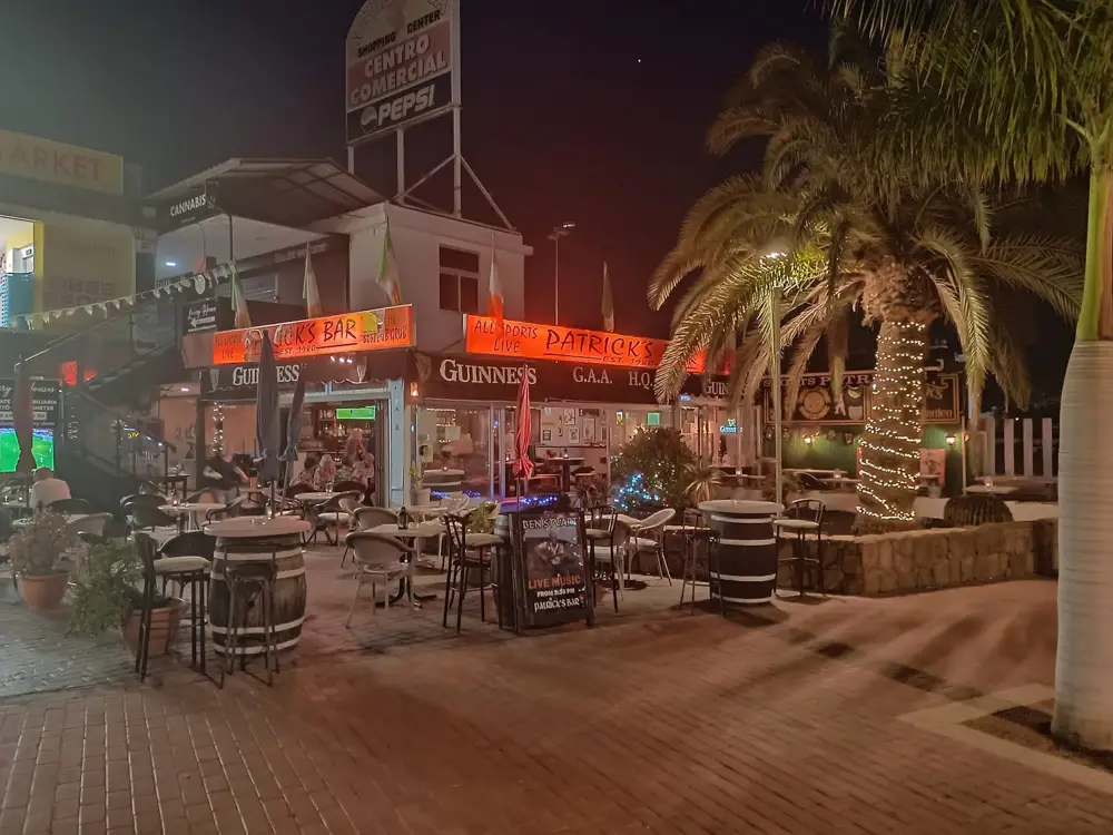 Terrasse im Einkaufszentrum Águila Roja bei Nacht, mit beleuchteten Palmen und Live-Musik-Schild
