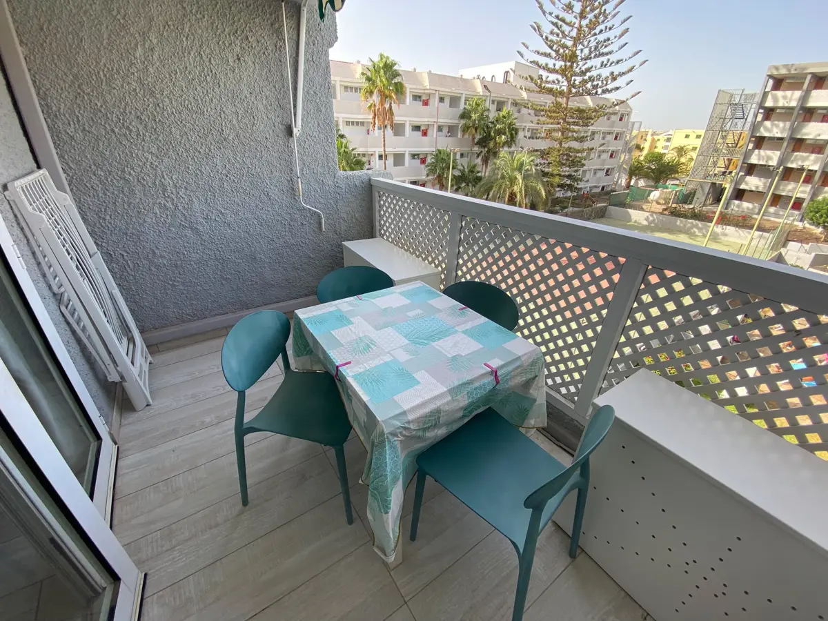 Balkon mit Tisch und vier Stühlen, Klappliege und weißem Gitter