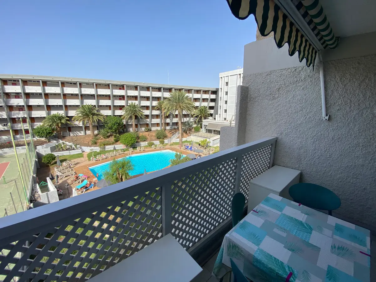 Balkon mit gestreifter Markise, Tisch und Stühlen, Blick auf den von Palmen umgebenen Pool