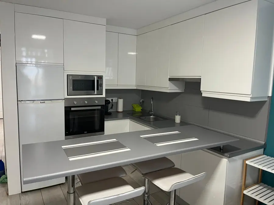 Weiße offene Küche mit Backofen, Mikrowelle und Theke mit Barhockern